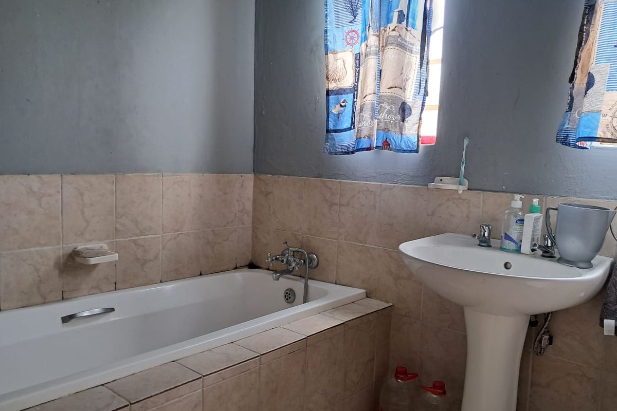A functional bathroom featuring a built-in bathtub and a pedestal washbasin with tiled splashbacks, requiring cosmetic updates to improve its overall condition.