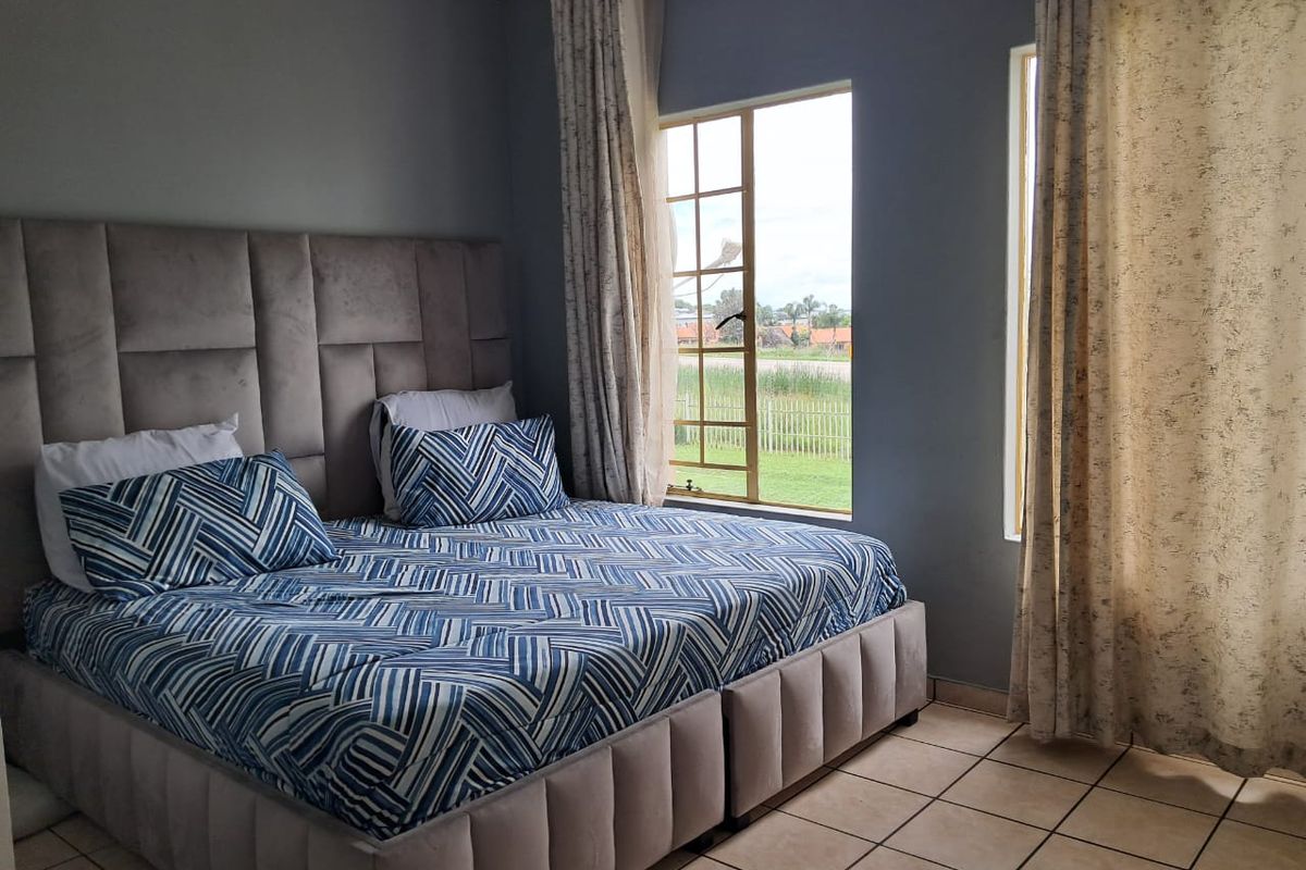 A well-lit bedroom featuring tiled flooring and large windows that provide natural light and views of the surrounding area.