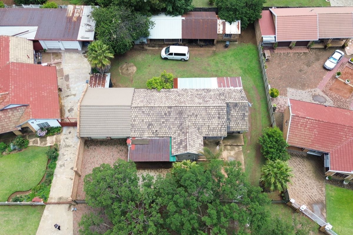 Aerial view of the property showing the main dwelling with tiled roofing, paved driveway, and surrounding garden area.