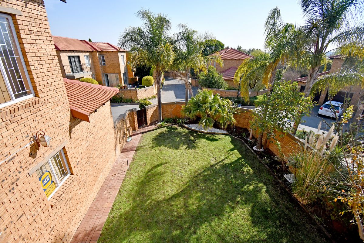 Elevated view of a private rear garden featuring a well-maintained lawn, paved pathway, and established landscaping within a secure townhouse complex.