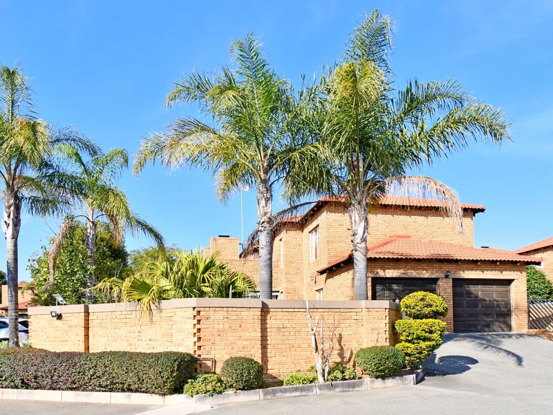 Front view of a face brick townhouse featuring a double garage, tiled roof, and a private brick boundary wall with established palm trees.