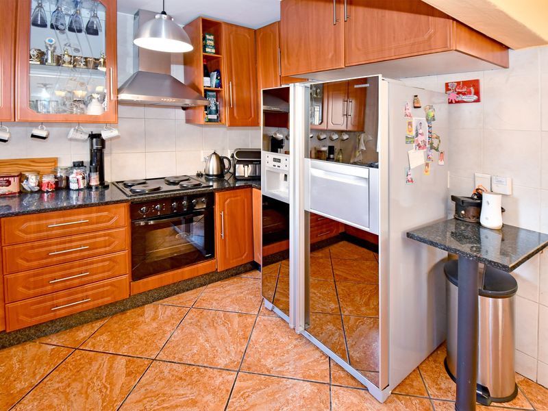 A functional kitchen featuring warm-toned wooden cabinetry, granite countertops, a built-in oven and hob, and tiled flooring throughout.