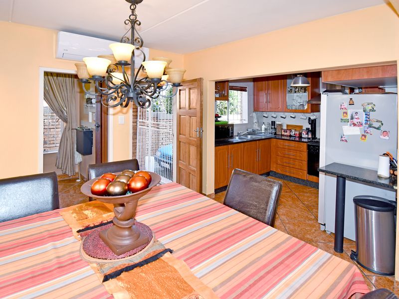 Open-plan dining area featuring a chandelier and split-system air conditioner, flowing into a functional kitchen with wooden cabinetry and granite countertops.