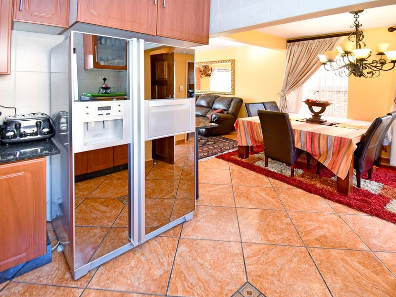 Open plan kitchen and dining area featuring tiled flooring, wooden cabinetry, granite countertops, and a traditional chandelier lighting fixture.