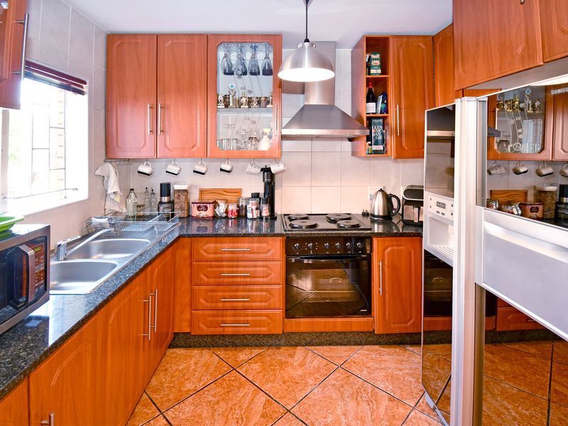 A functional kitchen featuring warm-toned laminate cabinetry, granite countertops, a double stainless steel sink, and integrated cooking appliances with tiled flooring.