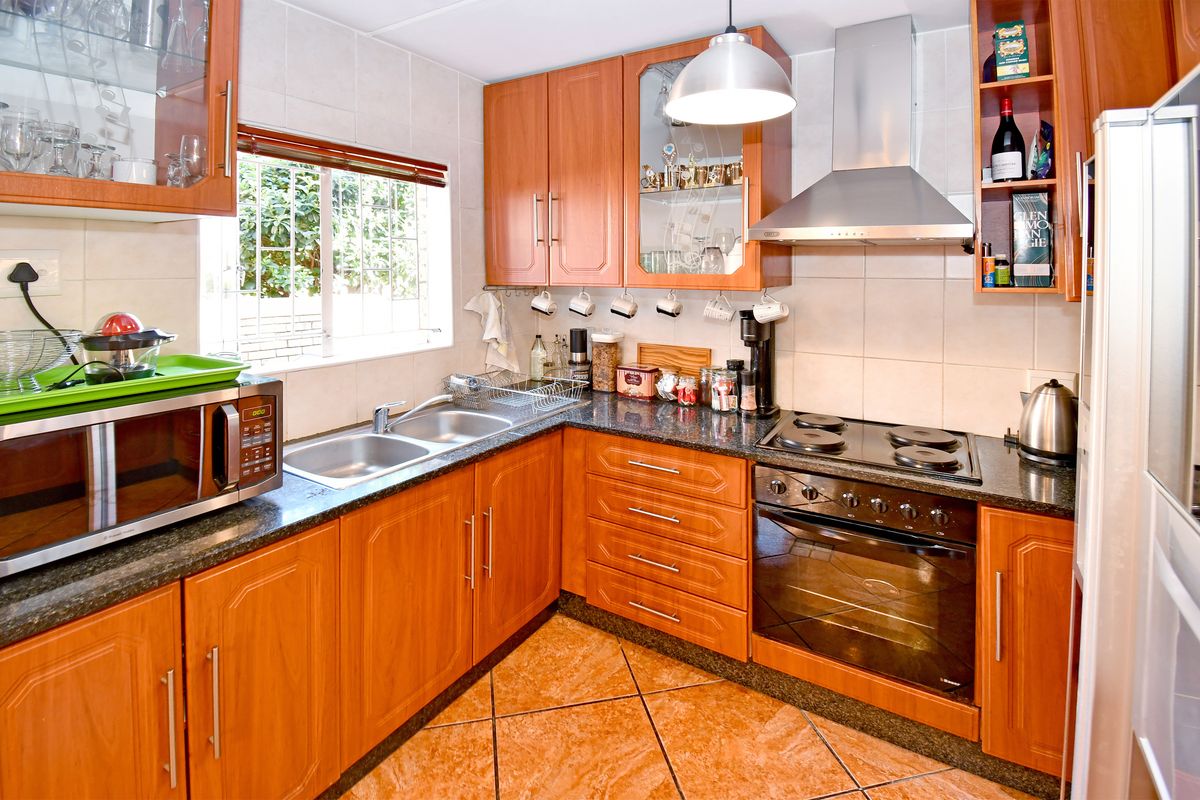A functional kitchen featuring wood-finish cabinetry, granite countertops, a built-in oven with hob, and a double stainless steel sink.