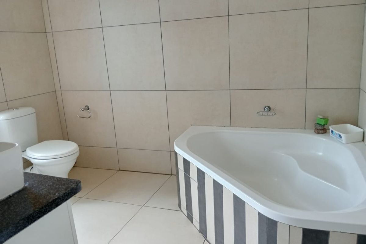 A functional bathroom featuring a corner bathtub, toilet, and vanity with tiled walls and flooring.