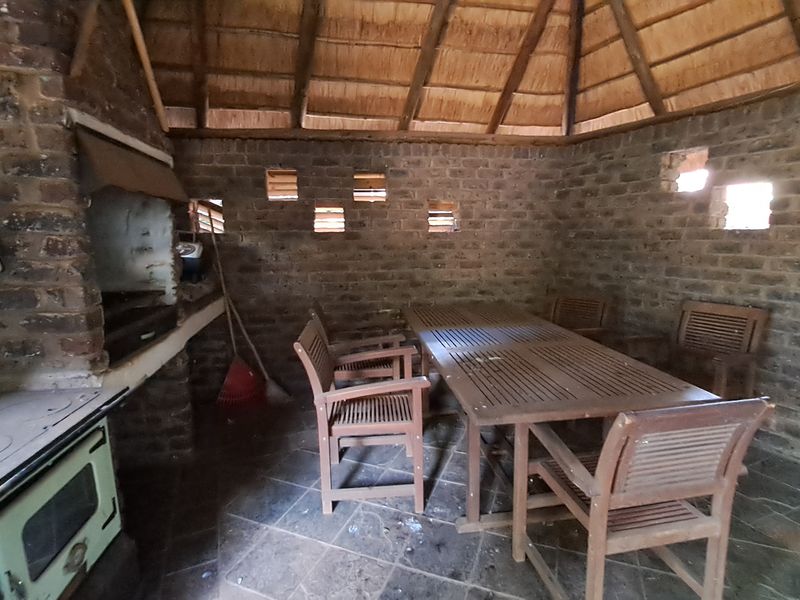 Covered outdoor patio area featuring a thatched roof, exposed brick walls, and a built-in braai, providing a rustic space for outdoor entertaining.