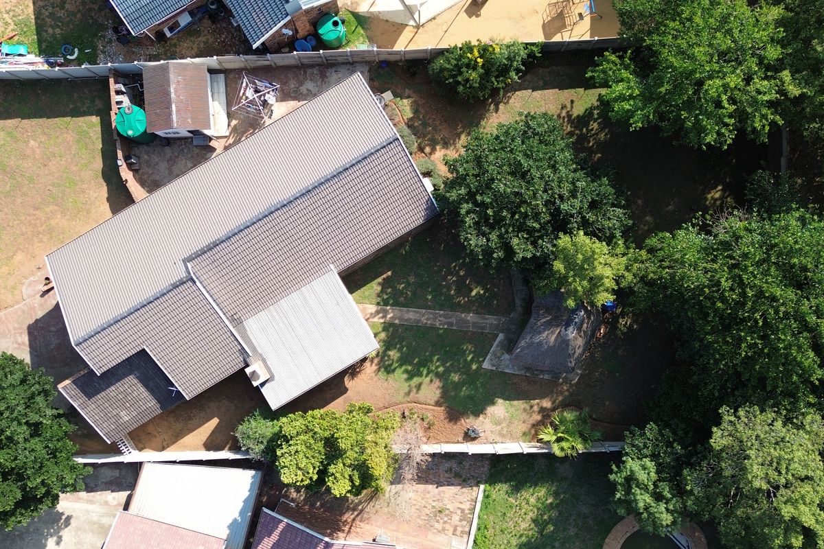 Aerial view of the property showing the main house with tiled and metal roofing, surrounding garden, perimeter wall, and a detached thatched lapa.