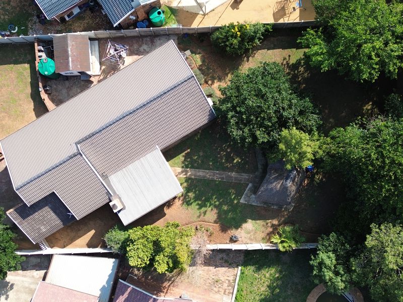 Aerial view of the property showing the main house with tiled and metal roofing, surrounding garden, perimeter wall, and a detached thatched lapa.