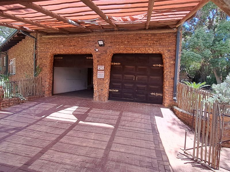 A double garage with brick facade and paved driveway, featuring a covered outdoor area with weathered timber fencing and shade cloth roofing.