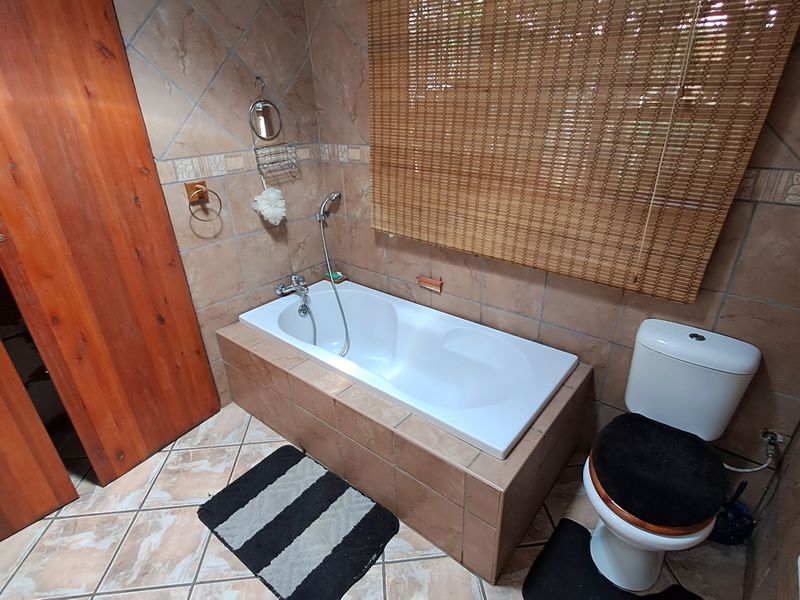 A functional bathroom featuring a built-in bathtub, ceramic tiling throughout, and a standard toilet suite.