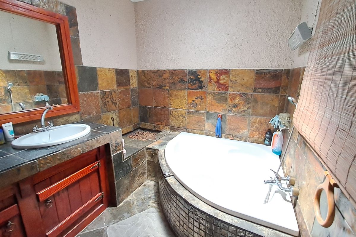 A bathroom featuring a corner bathtub, built-in vanity with basin, and rustic slate wall tiling throughout the space.