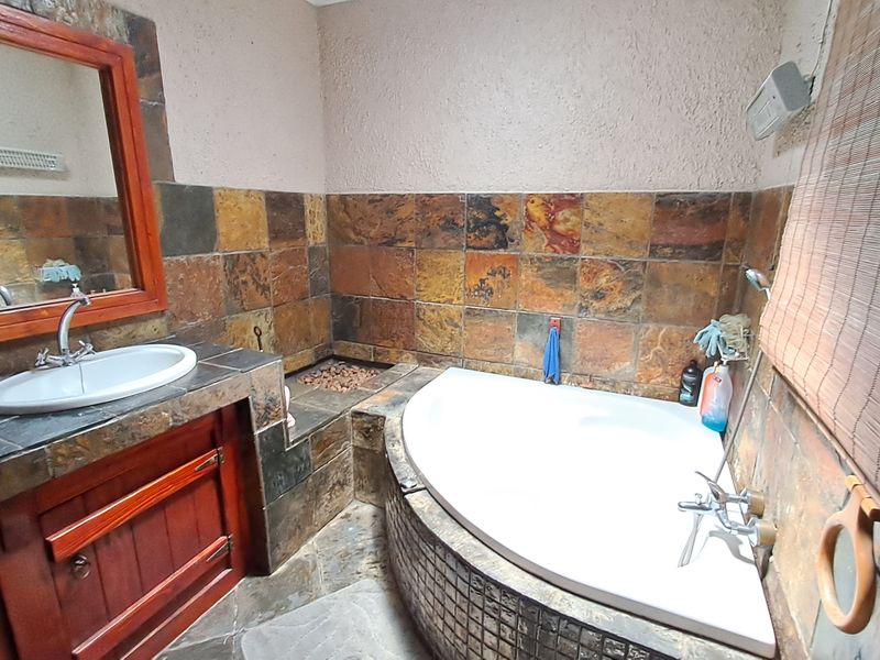 A bathroom featuring a corner bathtub, built-in vanity with basin, and rustic slate wall tiling throughout the space.