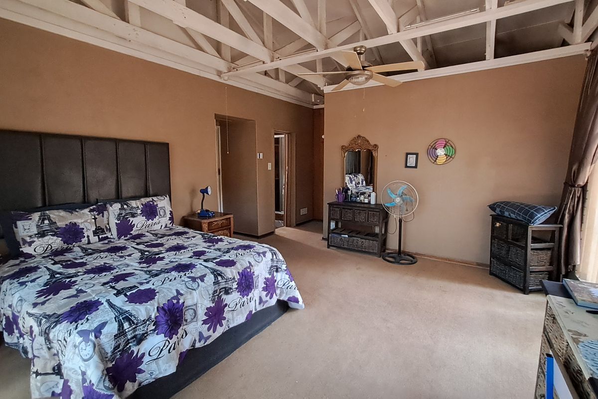 Spacious bedroom featuring exposed timber roof trusses, a ceiling fan, and neutral wall tones, offering a functional layout with potential for cosmetic updates.