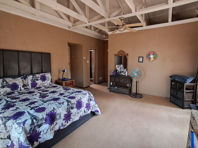 Spacious bedroom featuring exposed timber roof trusses, a ceiling fan, and neutral wall tones, offering a functional layout with potential for cosmetic updates.