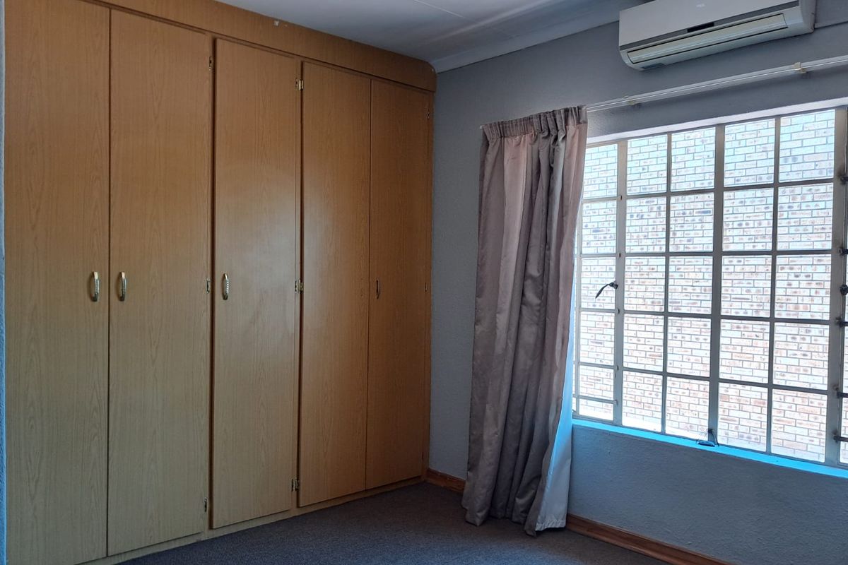 A clean, empty bedroom featuring built-in wooden cupboards, carpeted flooring, and a wall-mounted air conditioning unit.