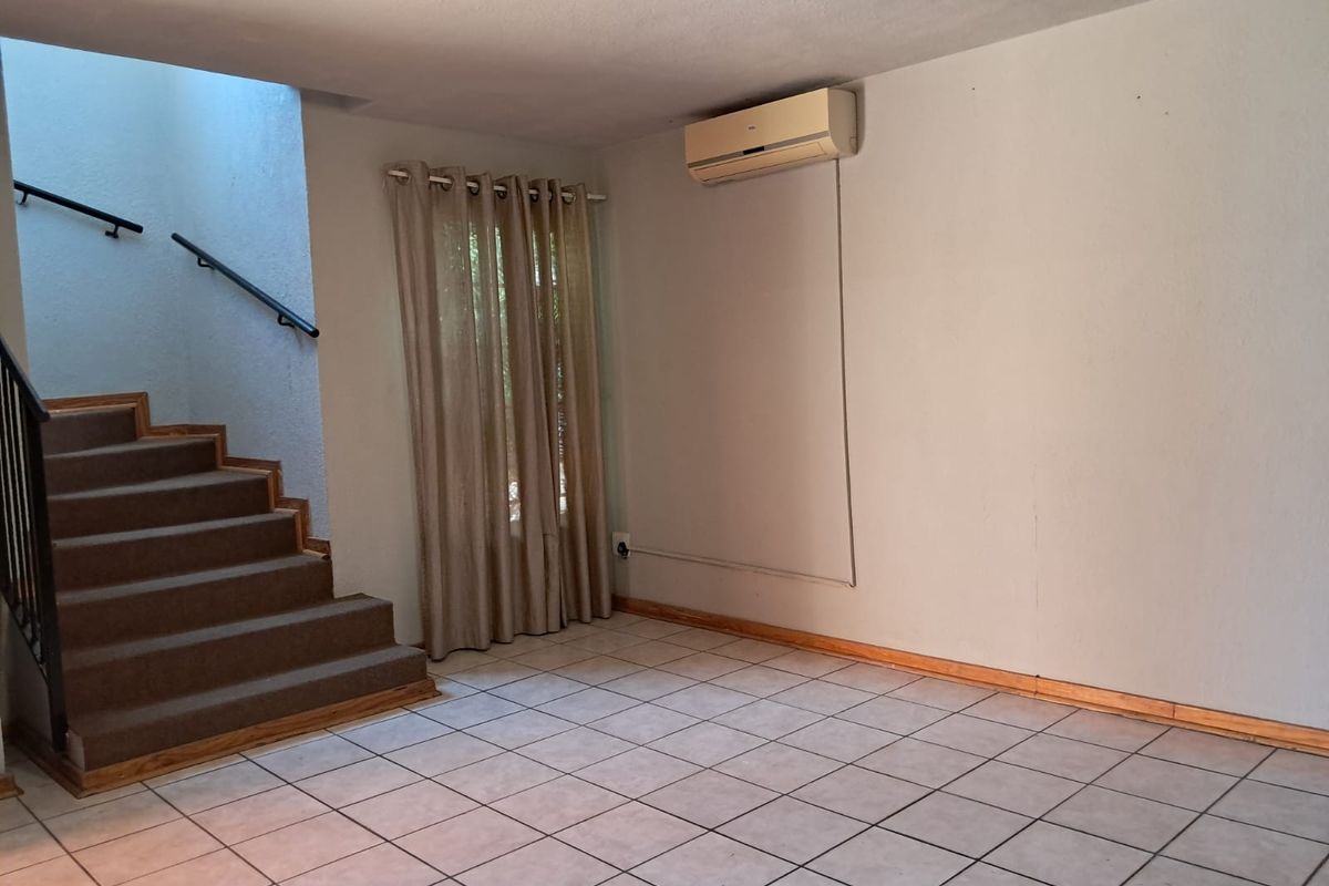 An empty living area featuring tiled flooring, a built-in staircase with a handrail, and a wall-mounted split-system air conditioner.