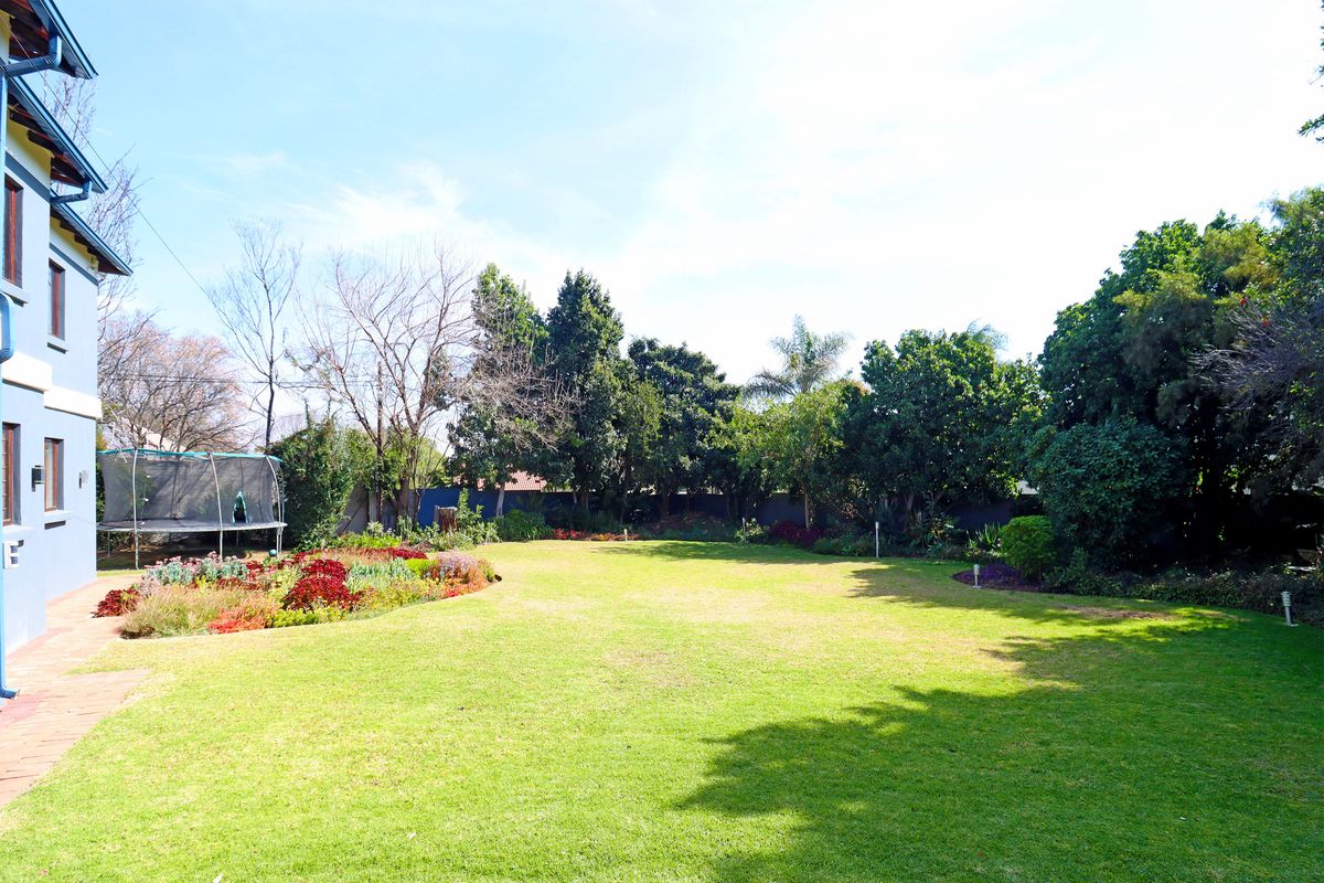 A spacious rear garden featuring a well-maintained lawn, established trees, landscaped flower beds, and a paved patio area adjacent to the house.