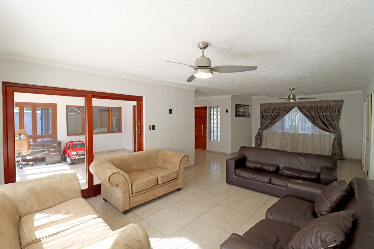 Spacious living room featuring tiled flooring, ceiling fans, and large sliding glass doors providing access to an adjacent sunroom area.