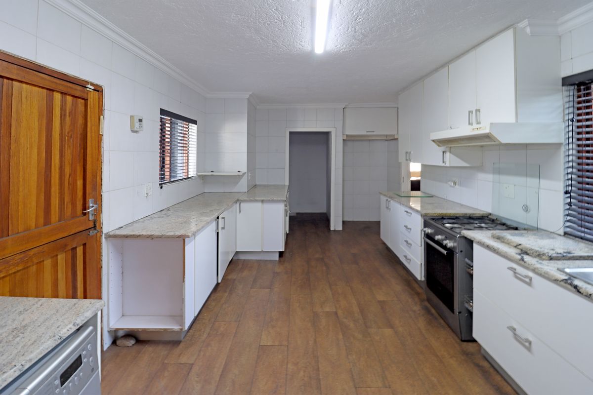 A functional kitchen featuring granite countertops, gas stove, extractor fan, and ample built-in cabinetry with a neutral tiled backsplash and laminate flooring.