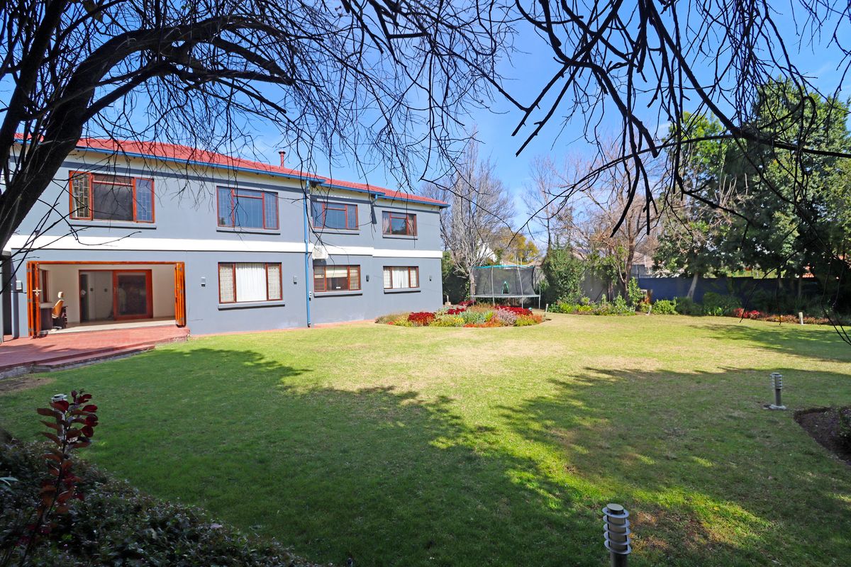 Spacious rear garden featuring a well-maintained lawn, landscaped flower beds, and a double-storey residence with a red tiled roof and patio access.