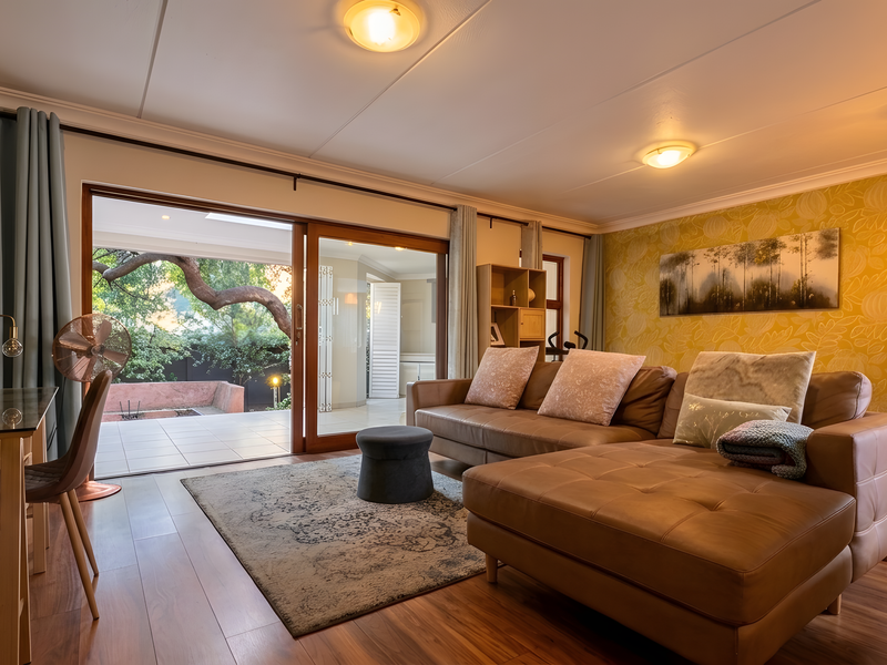 Spacious living room featuring warm laminate flooring, a decorative wallpaper accent wall, and large sliding glass doors providing seamless access to the outdoor patio area.