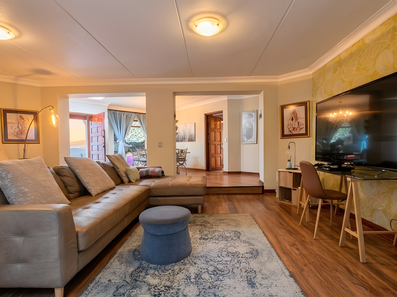 A well-maintained living room featuring laminate flooring, coved ceilings, and decorative wallpaper, with an open flow leading to an adjacent dining area.