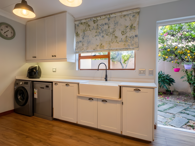 A well-appointed laundry room featuring shaker-style cabinetry, a farmhouse sink, and direct access to a private garden area.