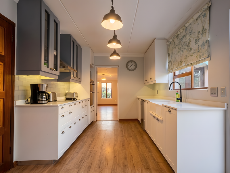 Modern galley-style kitchen featuring shaker cabinetry, quartz countertops, a farmhouse sink, and high-quality laminate flooring with direct access to the garden.