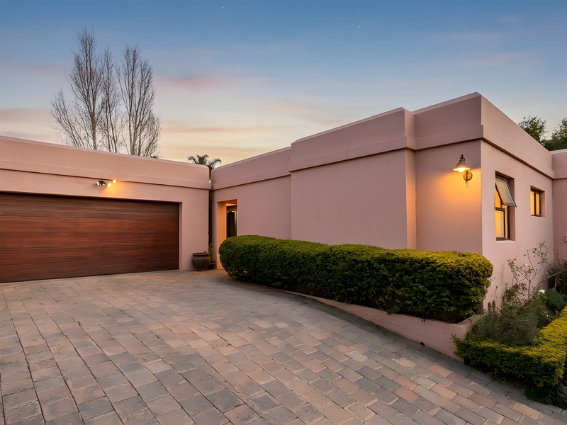 Front elevation of a townhouse featuring a paved driveway, integrated double garage with timber door, and exterior wall lighting.
