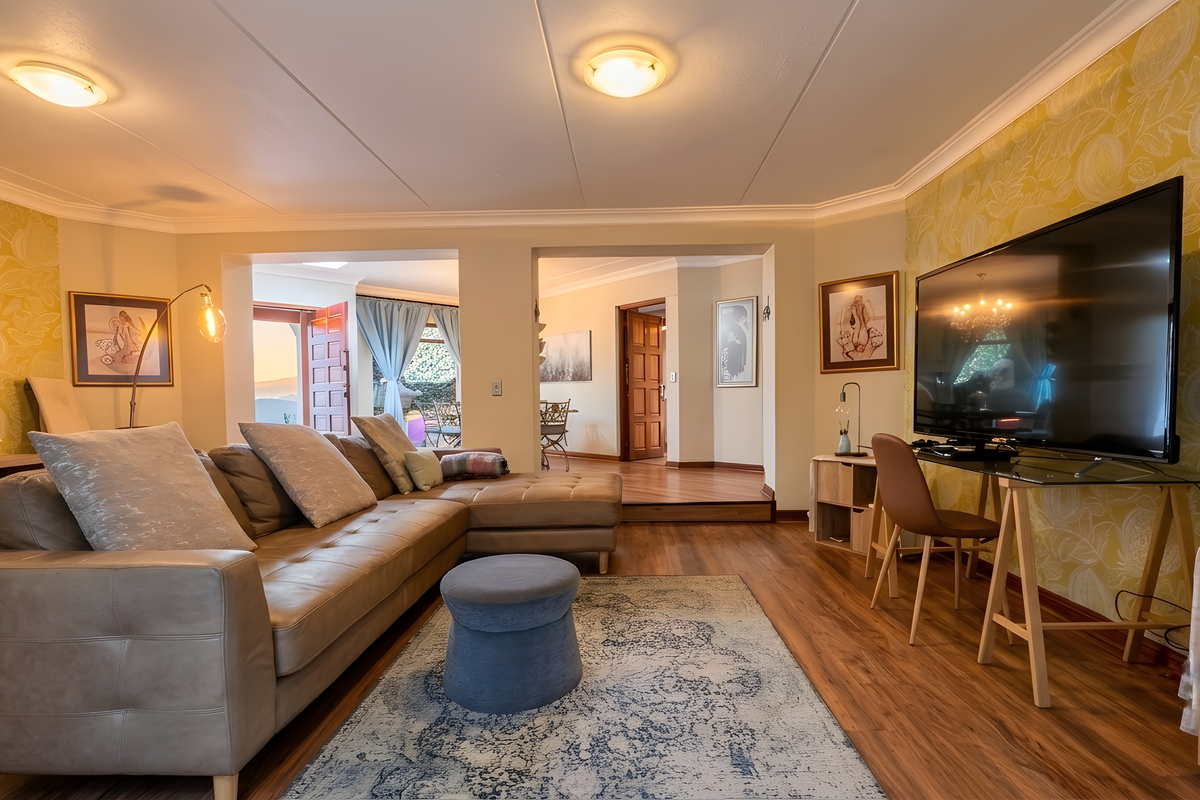 A well-maintained living room featuring laminate flooring, coved ceilings, and decorative wallpaper, with an open flow leading to an adjacent dining area.