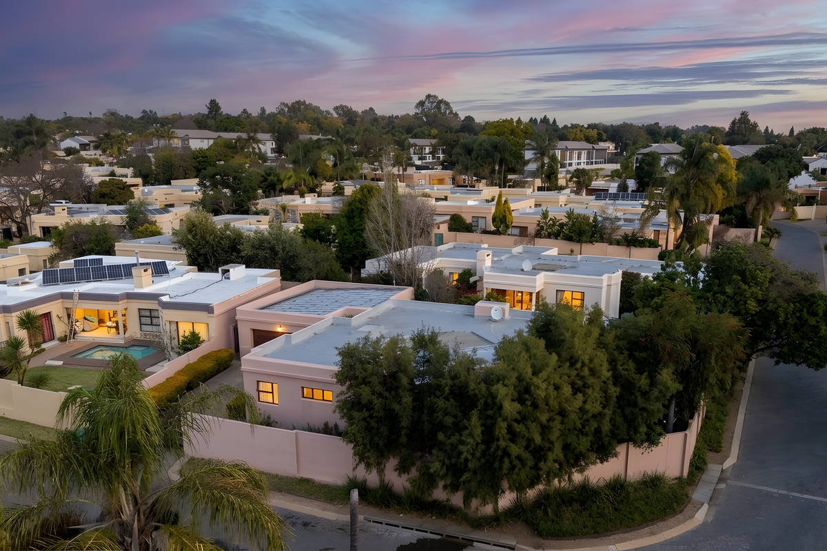 Aerial view of a residential townhouse complex at dusk, showcasing multiple units with flat roofs, solar installations, and private swimming pools.