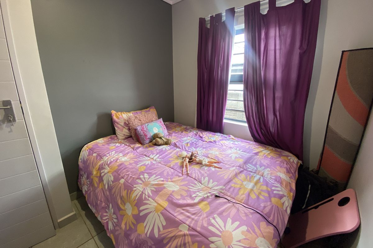 A compact bedroom featuring tiled flooring and a window fitted with security bars, finished with a neutral grey accent wall.