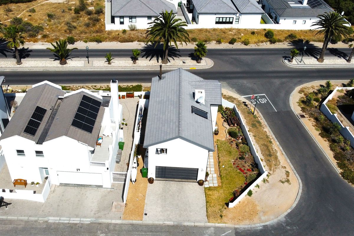 Aerial view of a residential property featuring a tiled roof with solar panels, a paved driveway, a garage, and a landscaped garden.