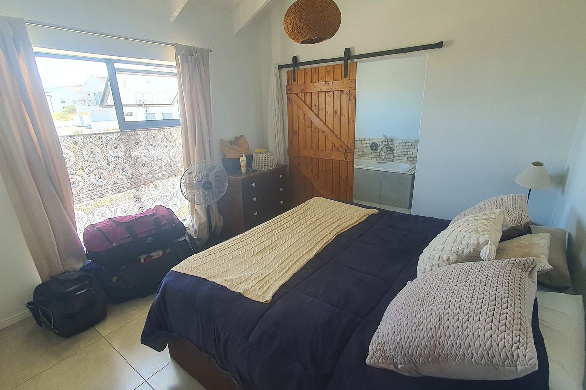 A bedroom featuring tiled flooring, exposed rafters, and a sliding barn door providing access to an en-suite bathroom.