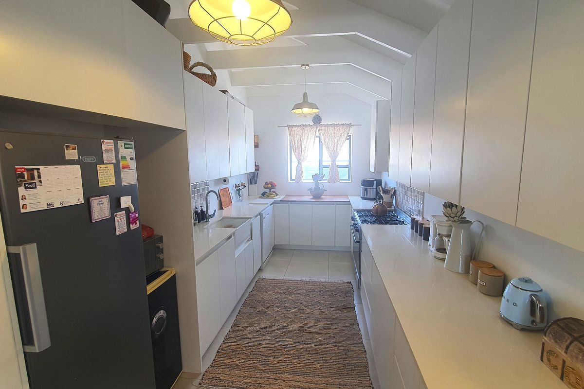 Modern galley-style kitchen featuring white cabinetry, quartz countertops, a farmhouse sink, gas hob, and exposed ceiling rafters.