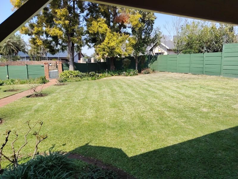 A well-maintained private garden featuring a manicured lawn, brick paved pathway, and secure perimeter fencing with a metal gate.