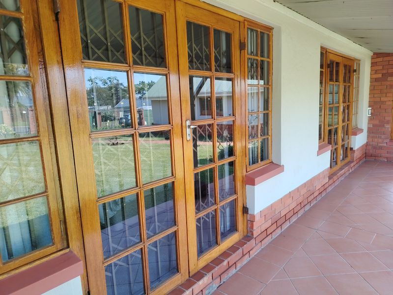 A covered patio area featuring tiled flooring, brick base detailing, and multiple wooden french doors with integrated security gates.