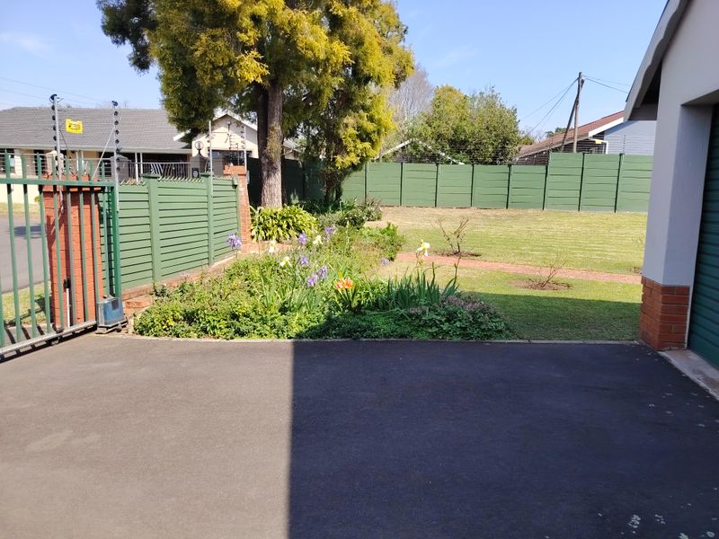 Front exterior view featuring a paved driveway, secure sliding gate with electric fencing, and a well-maintained garden area with brick pathways.
