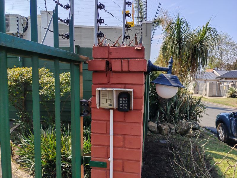 Close-up view of a brick entrance pillar featuring an integrated intercom system, keypad entry, and security lighting, protected by electric fencing.