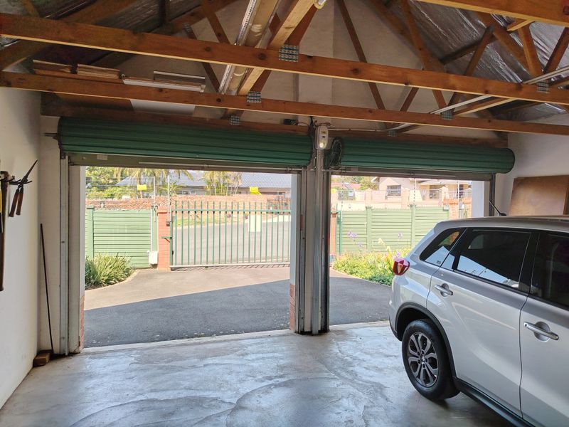 A functional double garage featuring exposed timber roof trusses, concrete flooring, and dual roller shutter doors opening to the driveway.