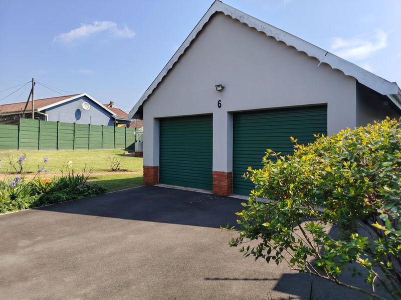 A well-maintained double garage featuring green roller doors, brick base accents, and a paved driveway, set within a neat residential garden.
