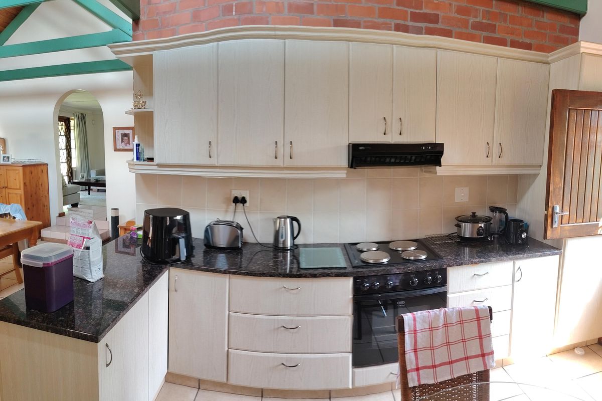 A functional kitchen featuring light-toned cabinetry, granite countertops, an integrated oven and hob, and a distinctive exposed brick wall with timber ceiling beams.