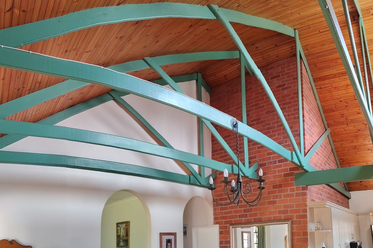 Spacious living area featuring high vaulted timber ceilings with exposed green trusses and a prominent brick fireplace feature wall.