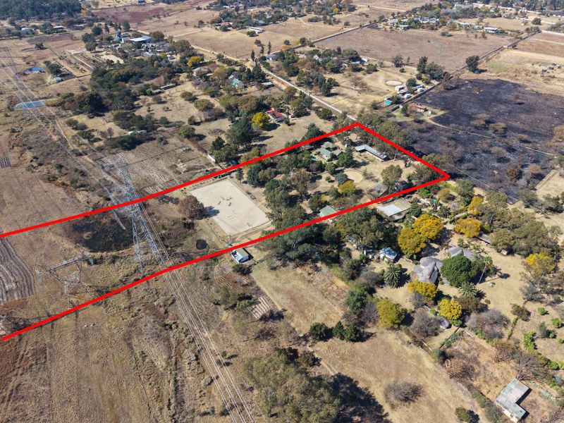 Aerial view of a large rural property featuring an equestrian arena, multiple outbuildings, and extensive grounds surrounded by natural landscape.