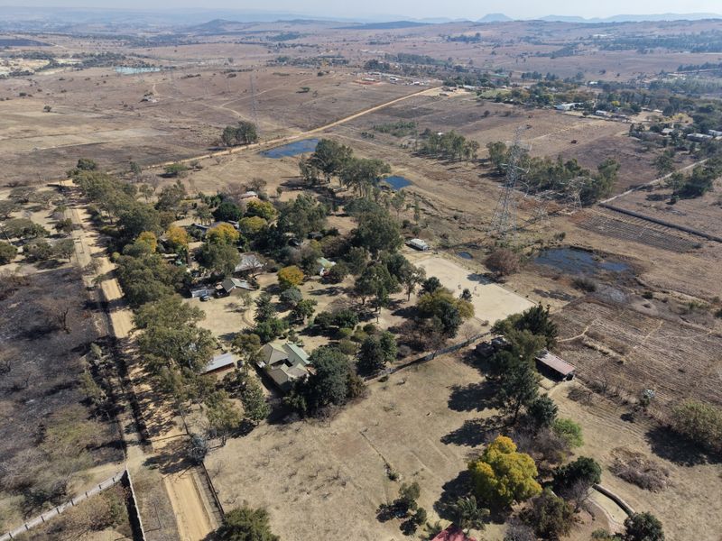 Aerial view of a large rural property featuring multiple structures, mature trees, and expansive surrounding land.