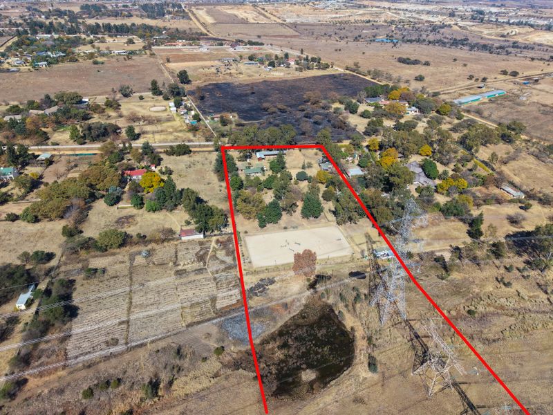 Aerial view of a large rural property featuring a fenced equestrian arena, mature trees, and expansive grounds within a semi-arid landscape.