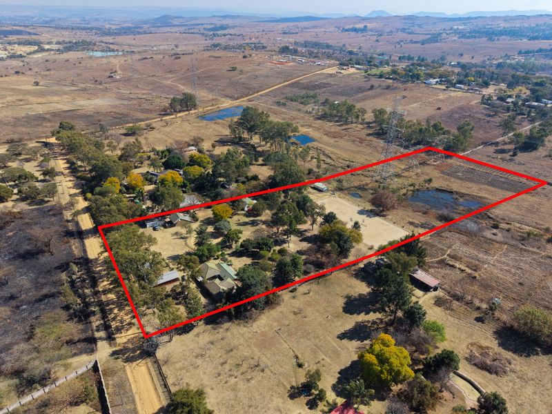 Aerial view of a large rural property plot with established trees, outbuildings, and surrounding landscape, highlighted by a red boundary outline.