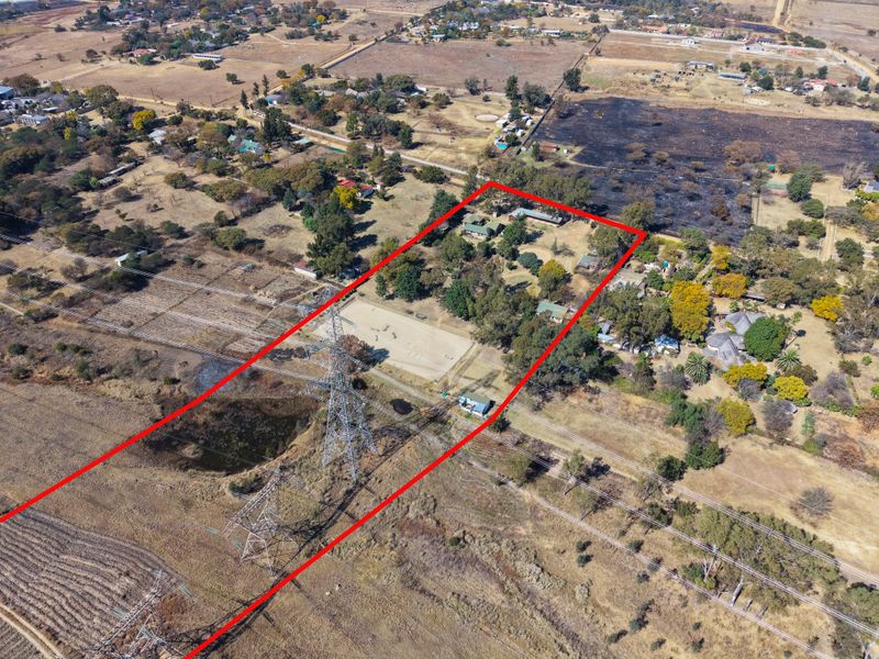 Aerial view of a large property plot featuring established trees, outbuildings, and prominent power line infrastructure crossing the land.